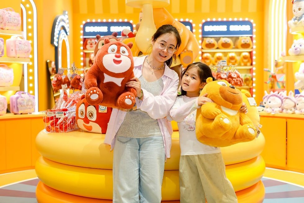Woman and child holding plush Boonie Bears toys in a colorful store at Xiaogan Fantawild Resort, surrounded by more plushies.