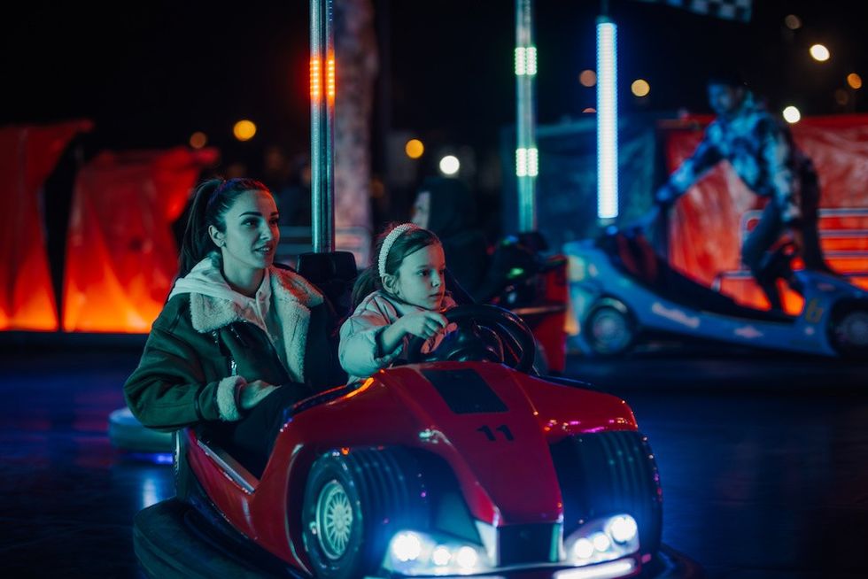 Woman and child in a red bumper car at an amusement park, lit by colorful lights.