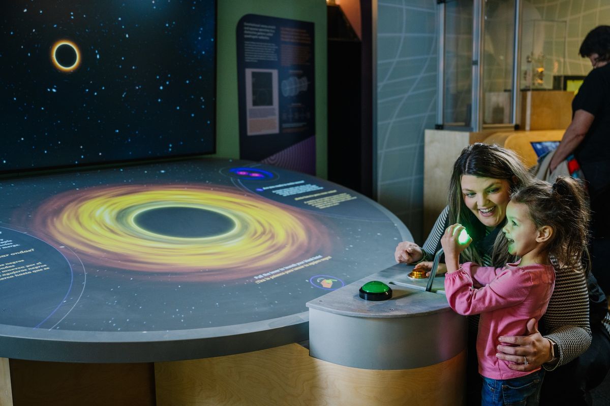 Woman and child interact with a black hole exhibit at a museum.