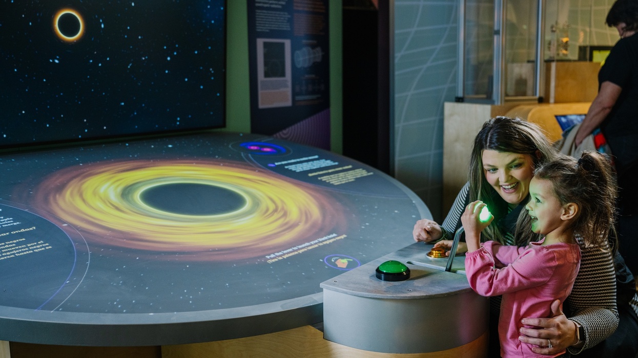 Woman and child interact with a black hole exhibit at a museum.