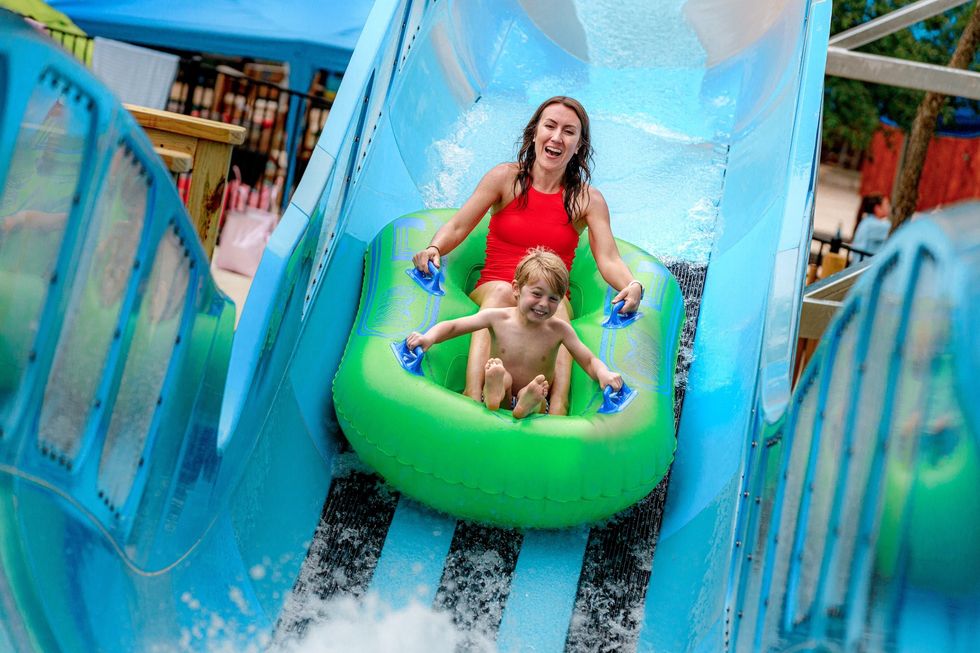 Woman and child joyfully sliding down a water slide on a green inflatable raft at Schlitterbahn New Braunfels