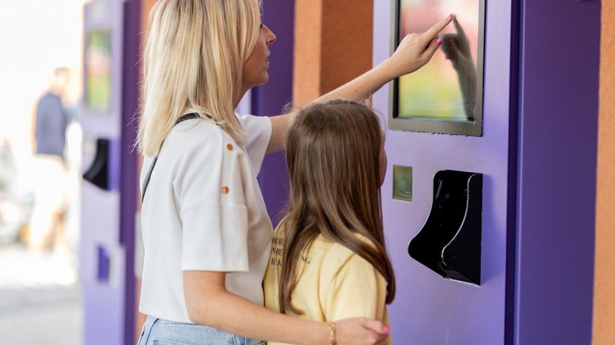 Woman and girl using a purple touchscreen kiosk outdoors.