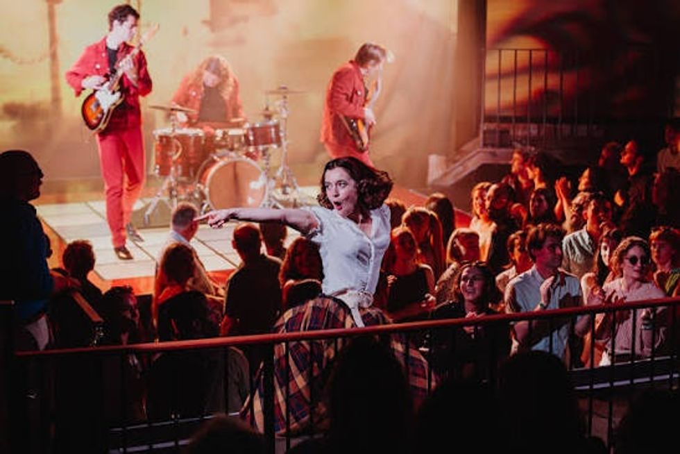 Woman dancing energetically in front of a band performing on stage, surrounded by a crowd.