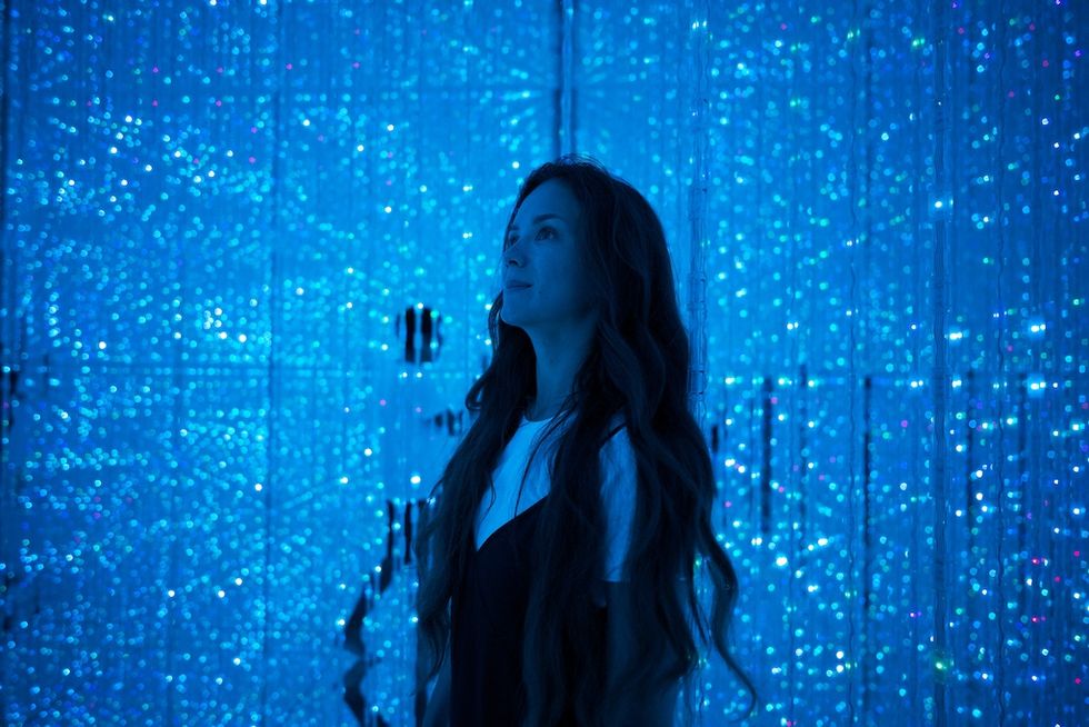 Woman gazes upward in a glowing blue room filled with shimmering lights.