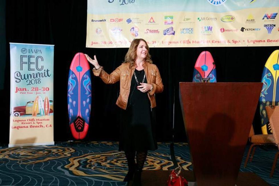 woman giving talk at iaapa fec summit with surfboards in background