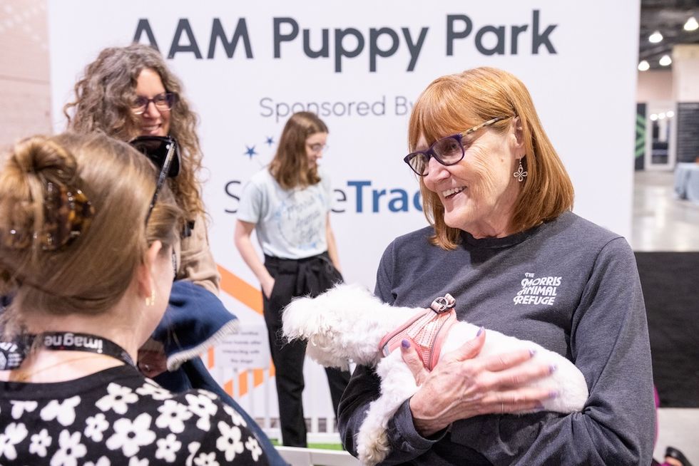 Woman holding a small white dog at AAM Puppy Park event.
