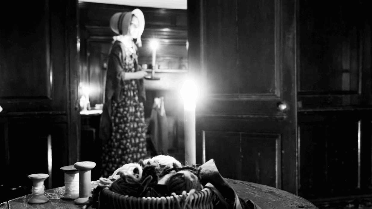 Woman holding candle in dark room at the Wordsworth Grasmere museum basket, with yarn on table in foreground.