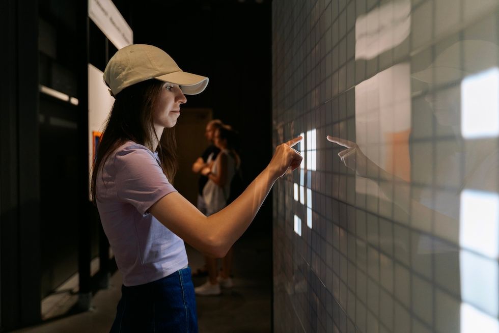 Woman in a cap interacting with an illuminated grid wall.