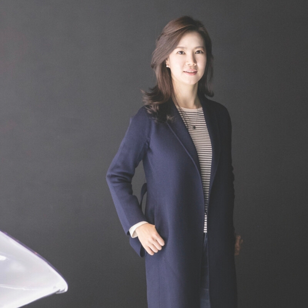 Woman in a navy coat and striped shirt, standing against a dark gray background.