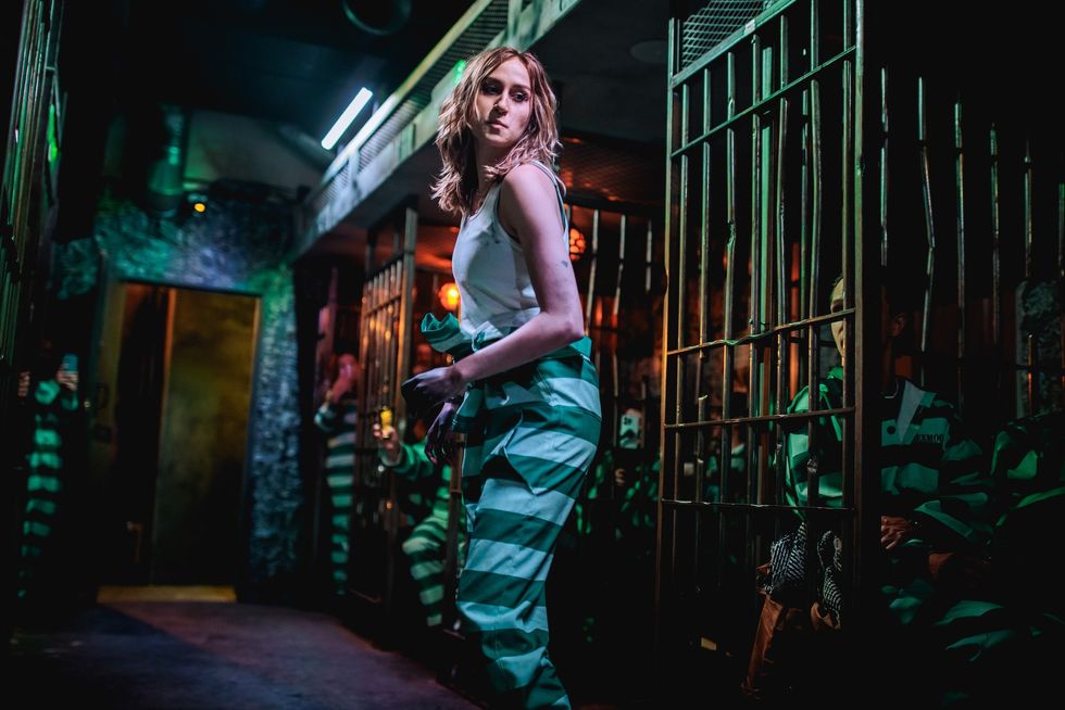 Woman in a prison escape room wearing striped pants, surrounded by cells.