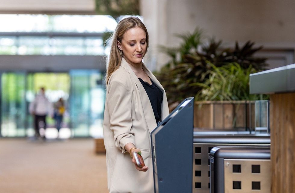 Woman in beige coat entering with keycard at an automated gate indoors.