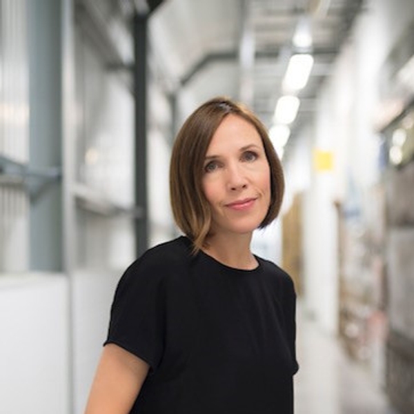 Woman in black shirt standing in a well-lit corridor.