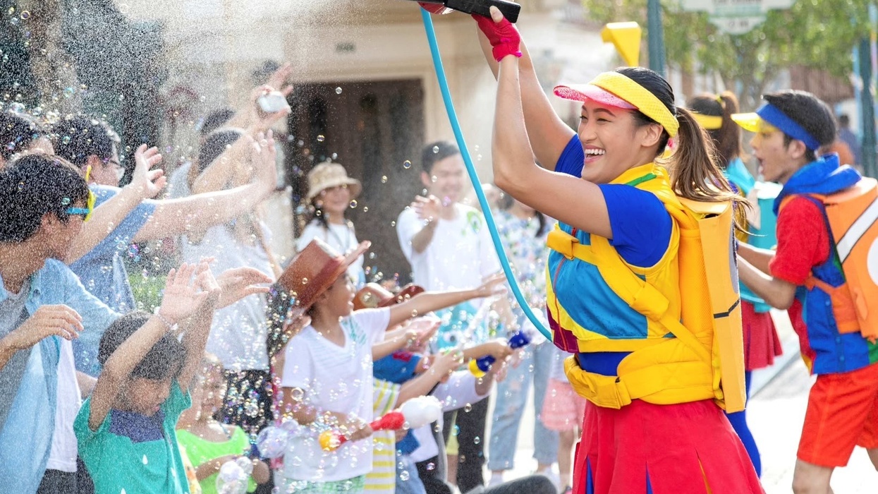 Woman in colorful outfit spraying water, crowd enjoying on a sunny day at Hong Kong Disneyland