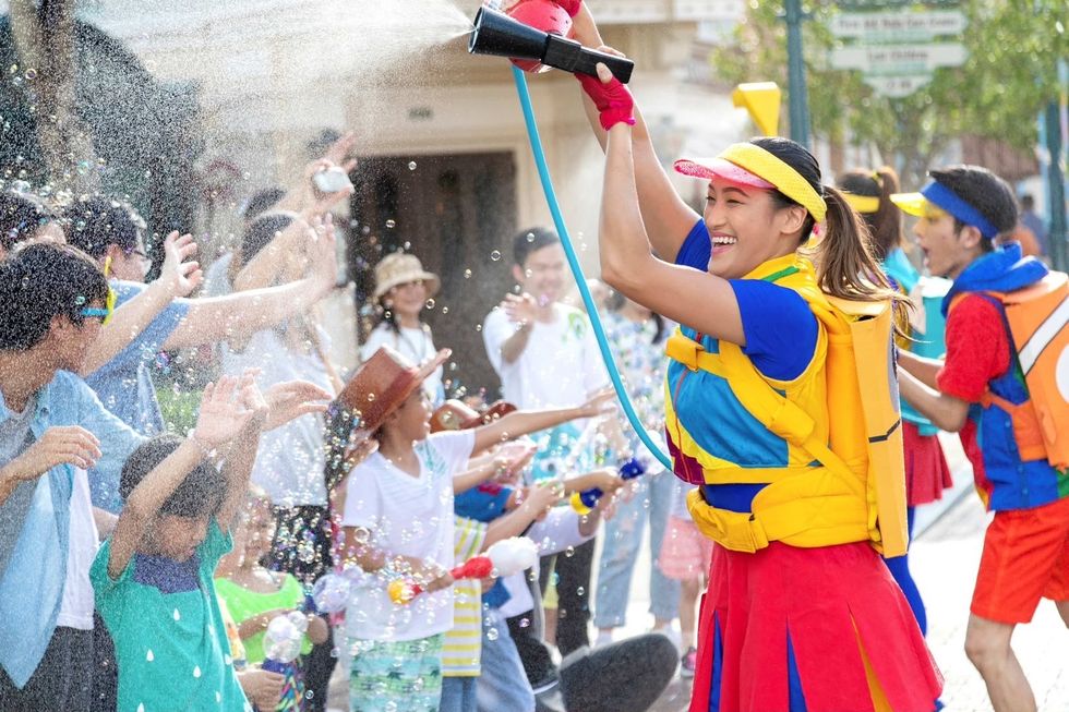 Woman in colorful outfit spraying water, crowd enjoying on a sunny day at Hong Kong Disneyland