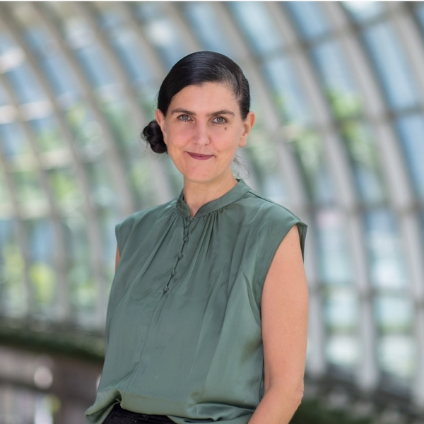 Woman in green blouse against a blurred, arched glass background.