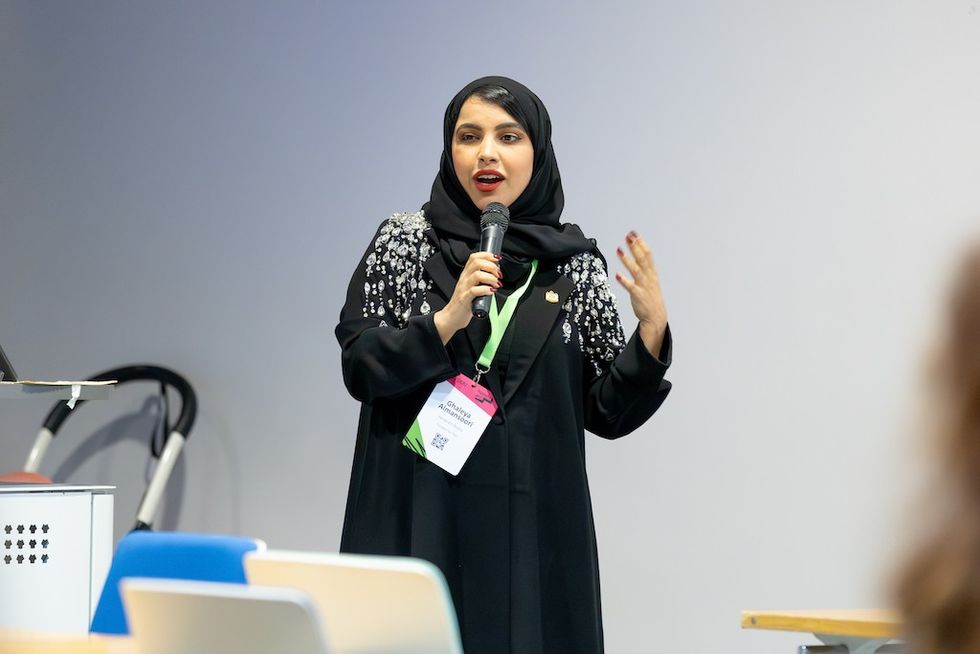 Woman in hijab speaking into a microphone at a conference.