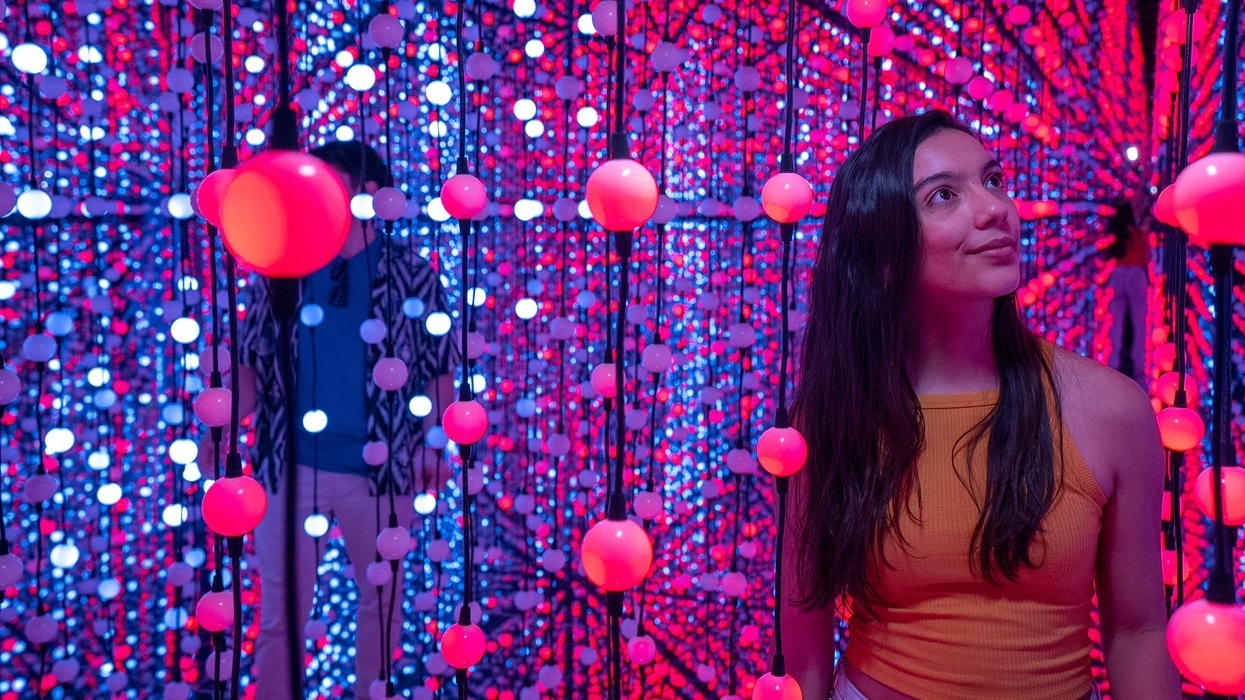 Woman in immersive space with hanging red and blue spheres, smiling upward.