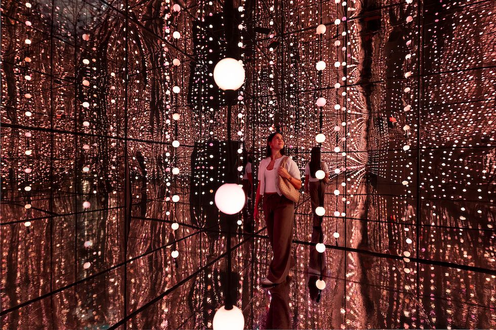 Woman in mirror room surrounded by hanging lights.