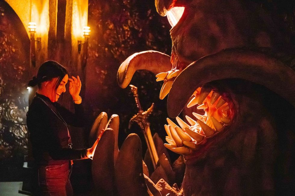 Woman interacts with a large monster sculpture, lit by warm, glowing lights.