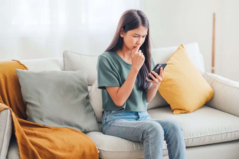 Woman looking concerned while reading a message on her phone, sitting on a cozy couch.
