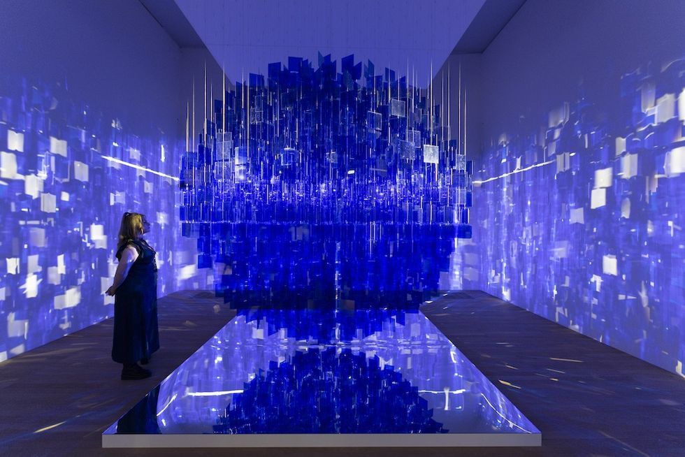Woman observing a blue geometric art installation with reflective surfaces.