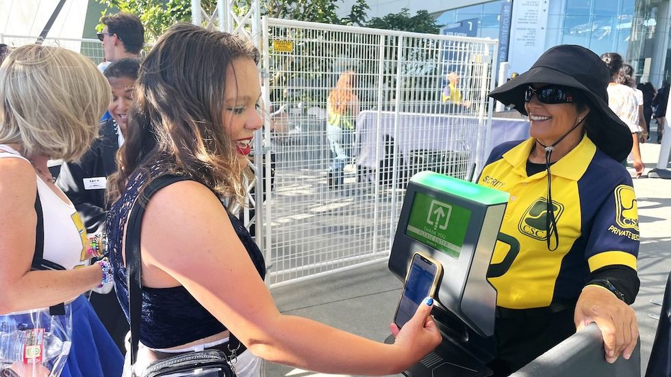Woman scans her phone ticket at an outdoor security checkpoint.