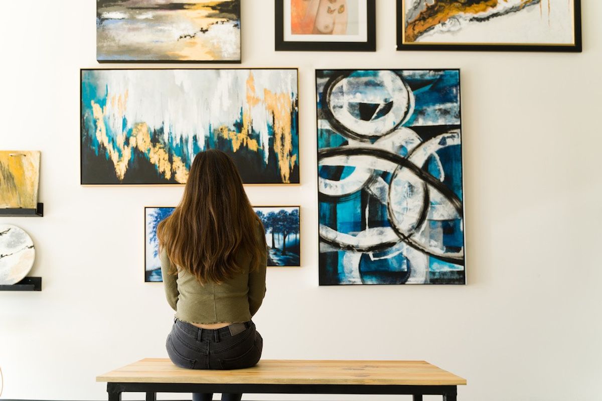 Woman sitting on a bench, viewing abstract art in a gallery.