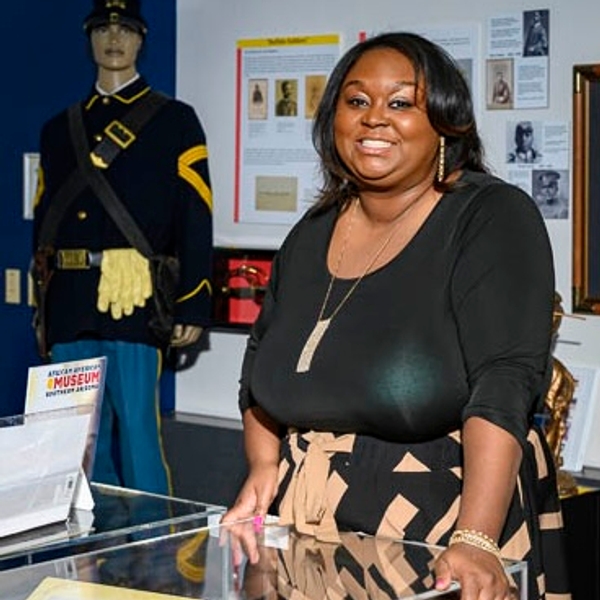 Woman smiling beside a museum exhibit with historical documents and a soldier mannequin.