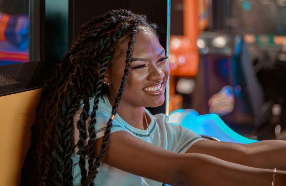 Woman smiling happily at an arcade, with colorful lights in the background.