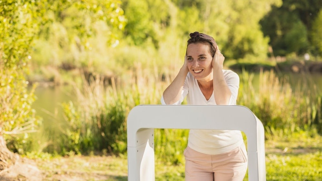 Woman smiling, holding ears, standing near white frame in sunny park.