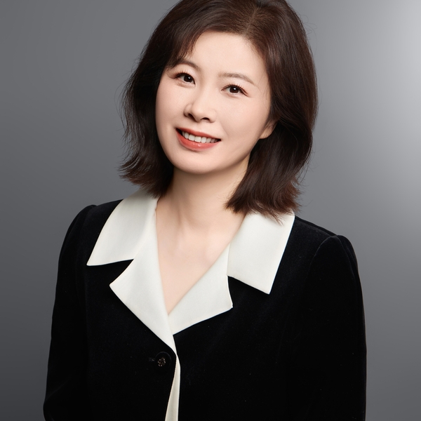 Woman smiling in a black and white collared outfit, gray background.