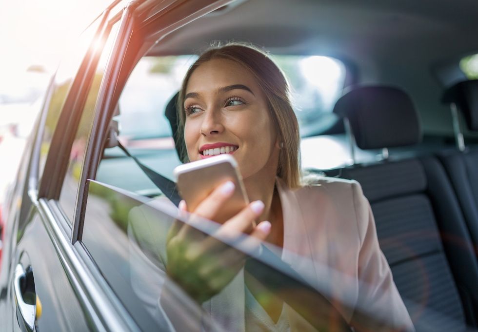 Woman smiling with a phone, looking out a car window.