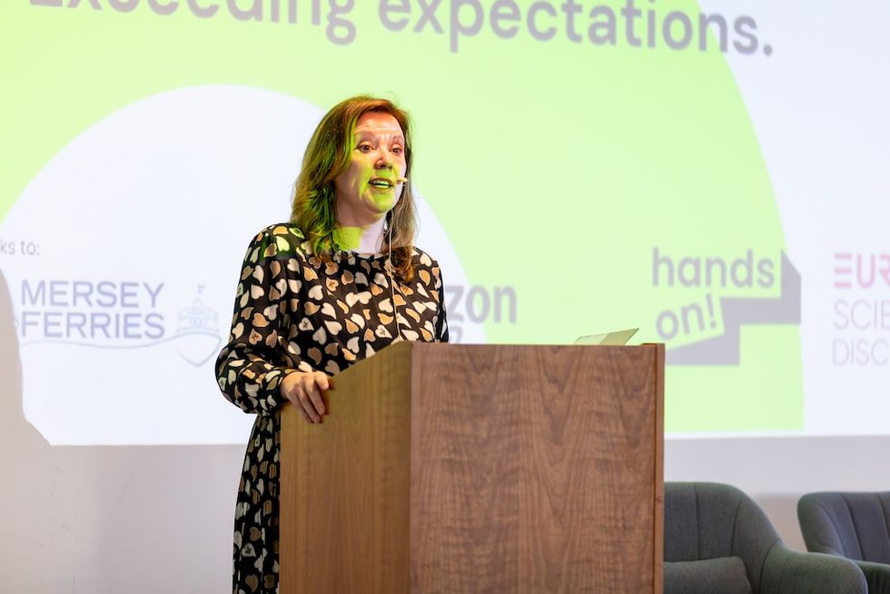 Woman speaking at a podium with a presentation behind her.