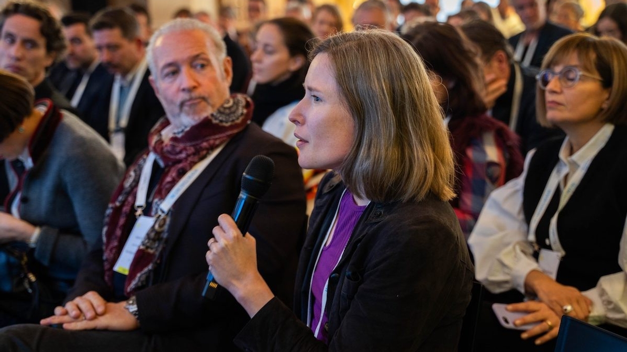 Woman speaks into a microphone at a conference, surrounded by attendees.