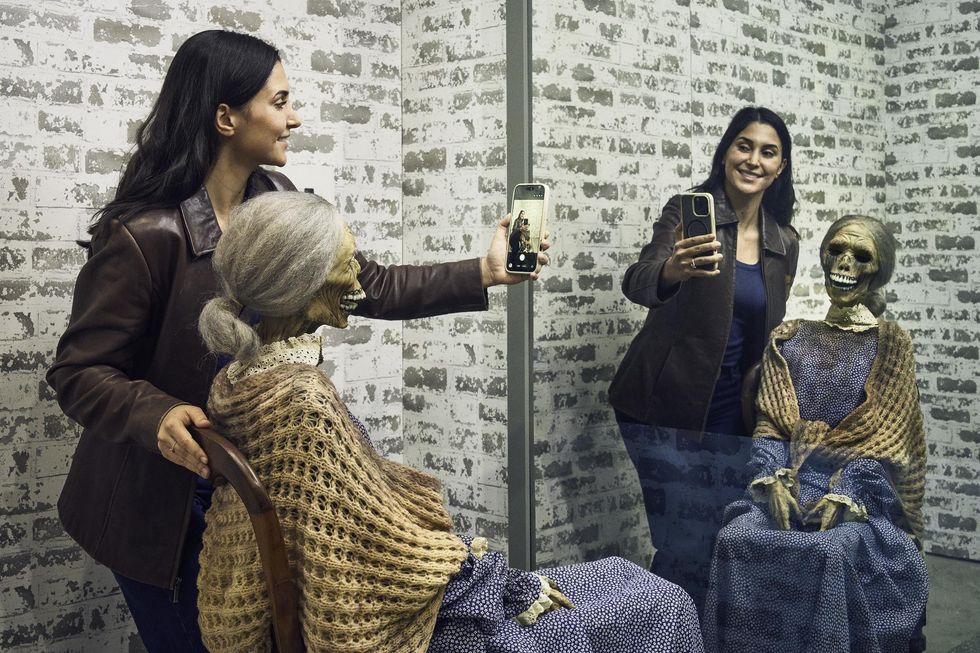 Woman taking a selfie with a skeleton reflection in the mirror at the Academy Museum