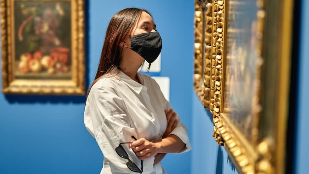 Woman visitor wearing an antivirus mask in the historical museum looking at pictures.