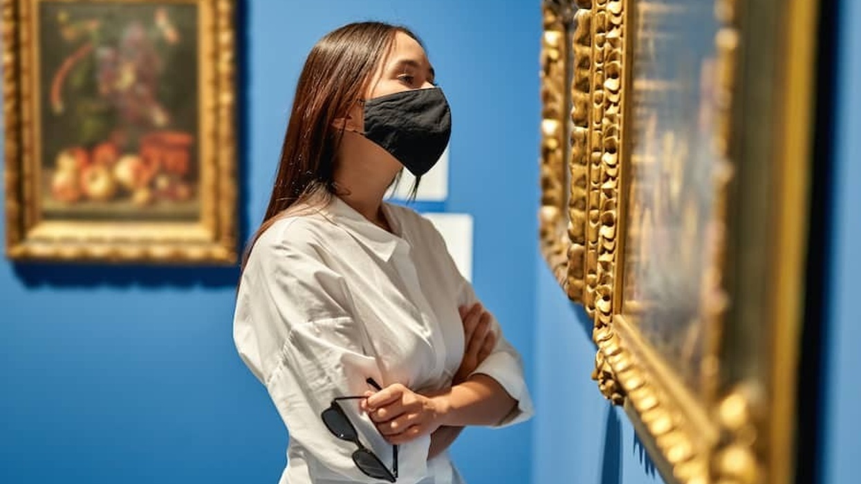 Woman visitor wearing an antivirus mask in the historical museum looking at pictures.