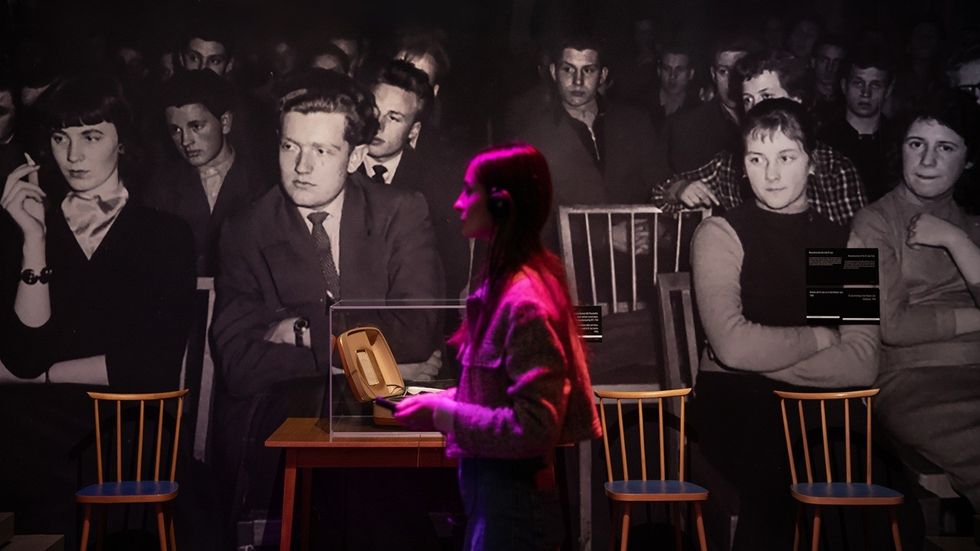Woman walks past a black-and-white mural of an audience and a small display on a table.
