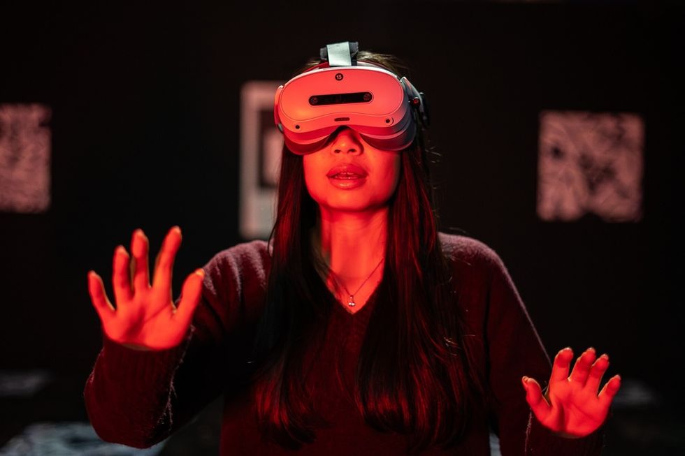 Woman wearing VR headset, hands raised, red lighting in The Mind of a Serial Killer: The Experience.