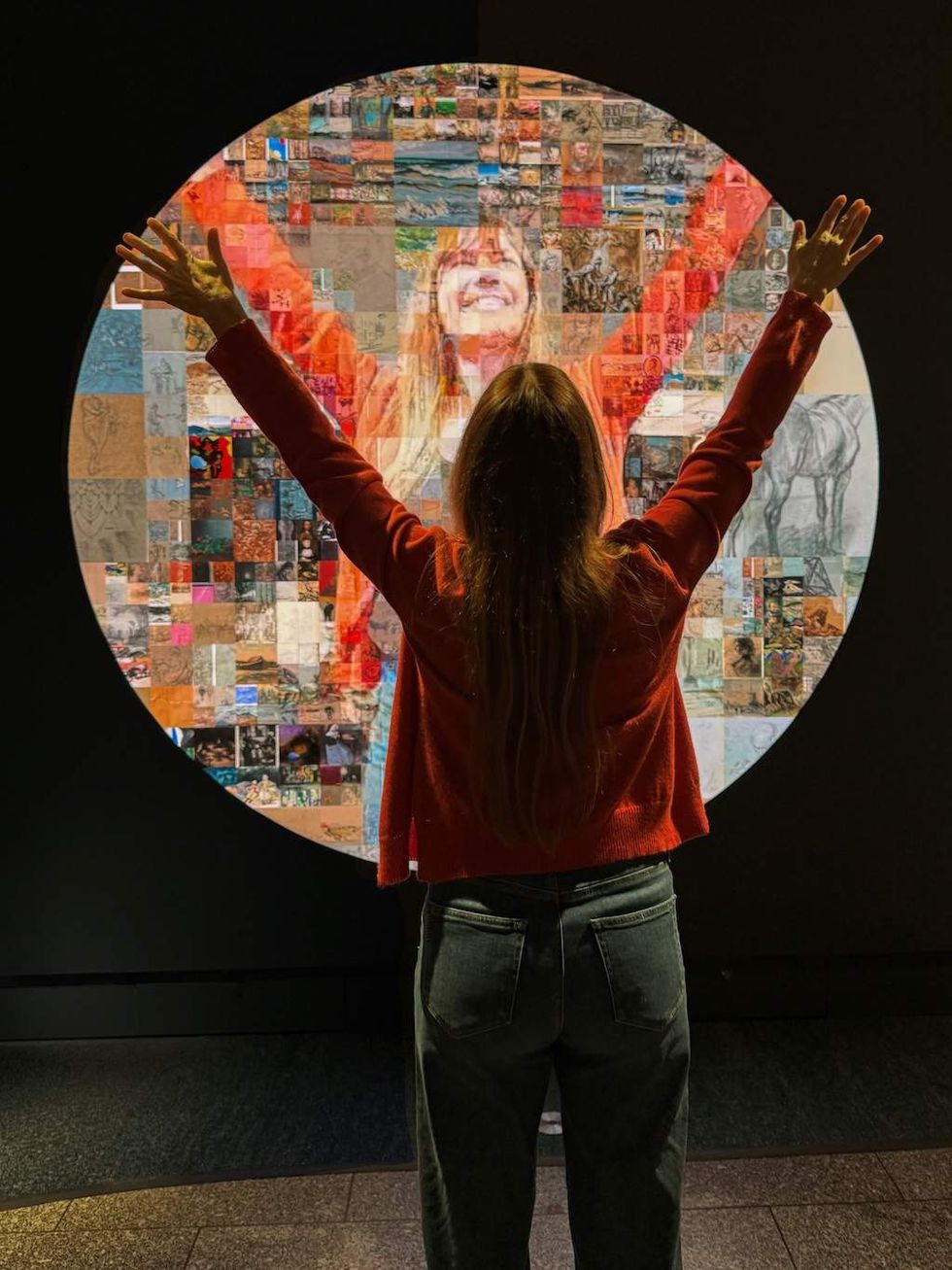 Woman with arms raised facing a colorful digital mosaic display.
