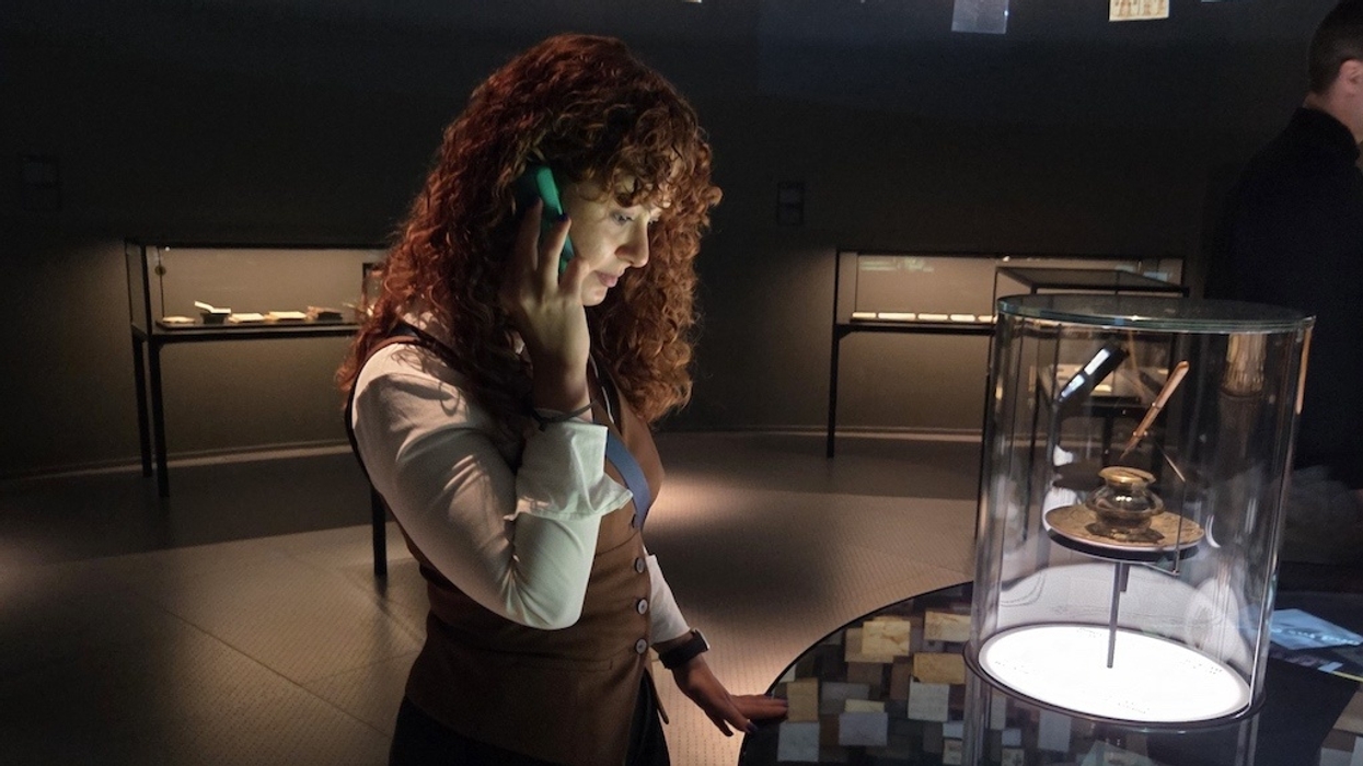 Woman with curly hair looks at an exhibit in a museum while holding a Guide-ID Podcatcher audio guide device