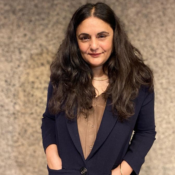 Woman with long hair in a blue blazer standing against a textured background.