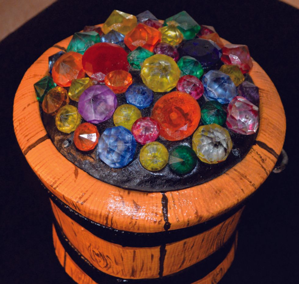 Wooden barrel filled with colorful, faceted gems on a dark background.