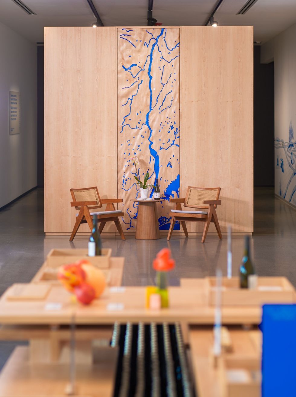 Wooden chairs and table with blue river design backdrop in a modern exhibition space.