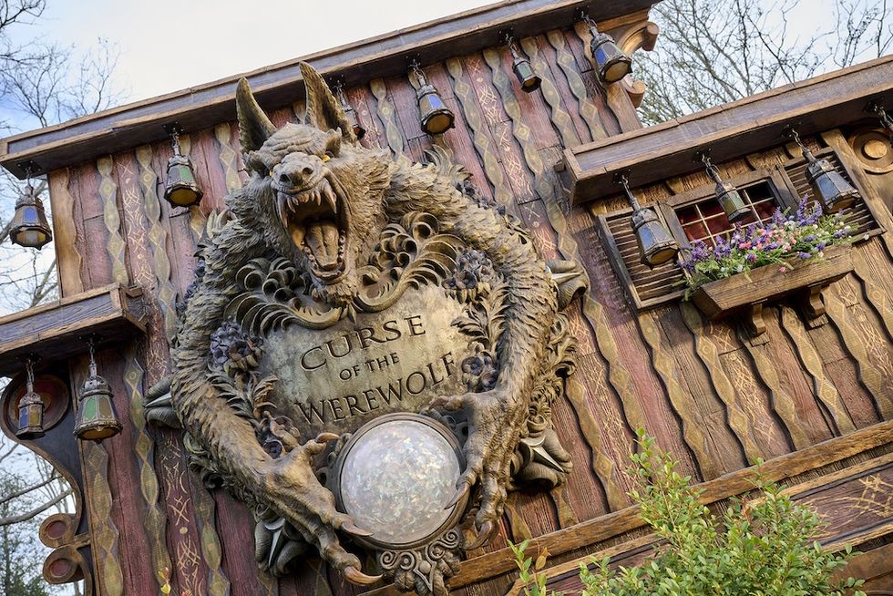 Wooden facade outside Epic Universe's Curse of the Werewolf ride, with a detailed werewolf sculpture and lanterns.