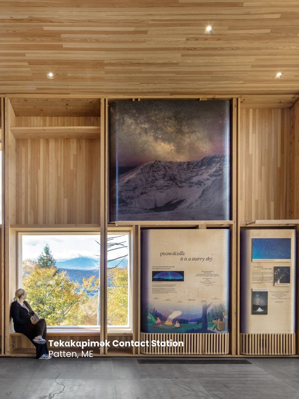 Wooden interior with large nature photos and a person seated by a window at Tek\u03b1k\u03b1pim\u0259k Contact Station.