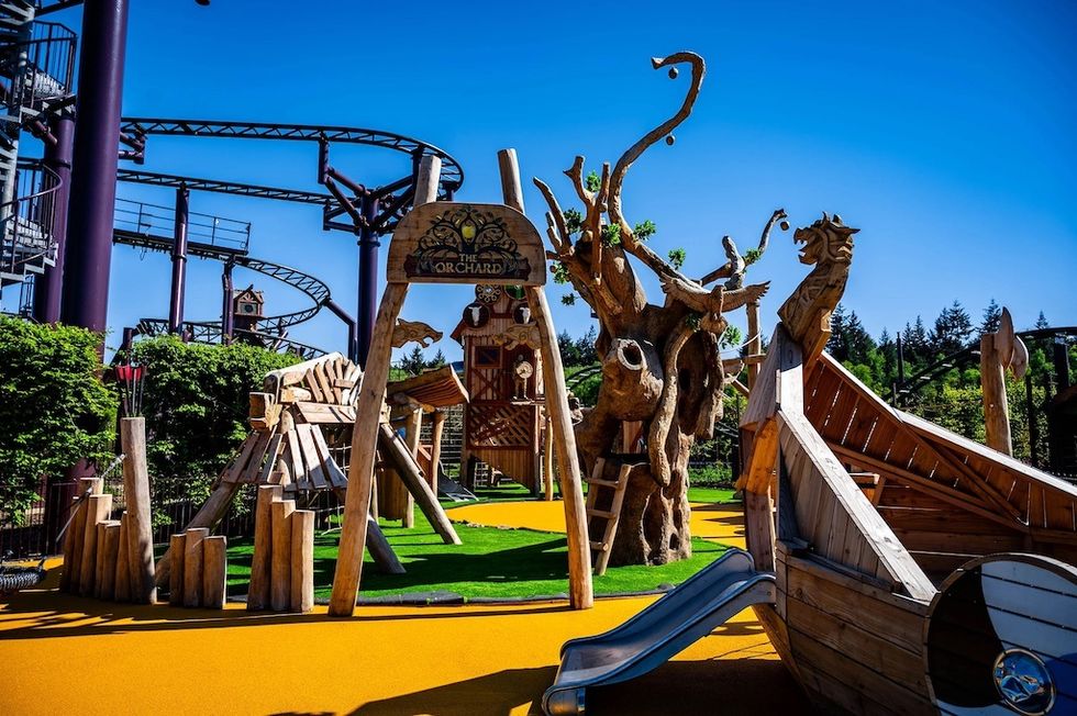 Wooden playground with slides and climbing structures under a clear blue sky.