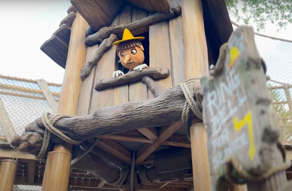 Wooden puppet peeks from a treehouse window, sign nearby reads "Ring Bell for Service" at Universal's DreamWorks land