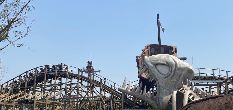 Wooden roller coaster with a ship inside a giant fish head structure, clear sky in the background.
