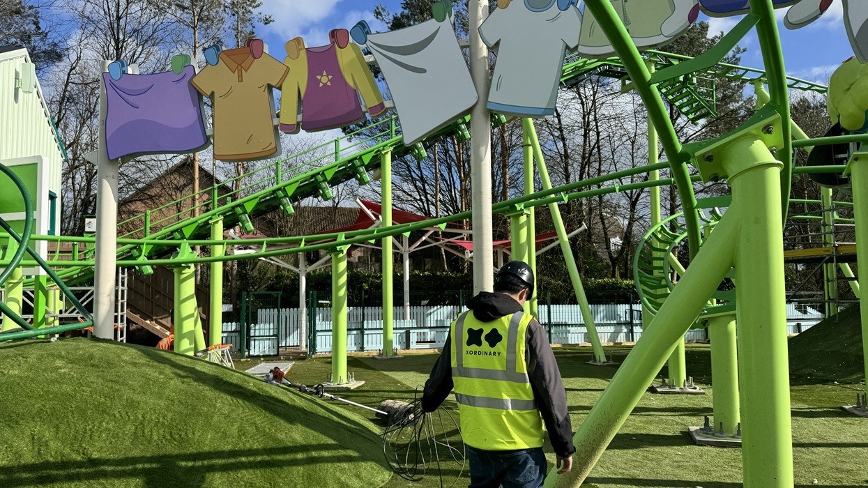 Worker in high-vis vest near colorful roller coaster and clothesline decor.